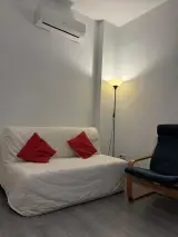 Salón del apartamento con sofá cama blanco, sillón azul, lámpara de pie y aire acondicionado en la pared